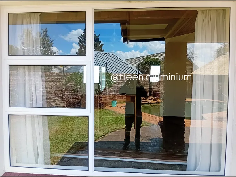 White aluminium sliding window looking onto a sunlit lawn